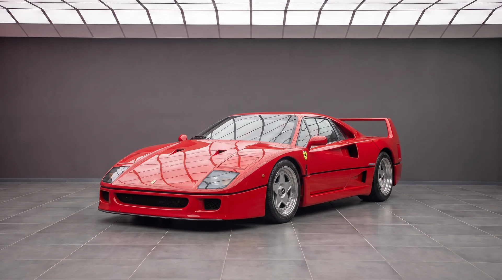 Ferrari F40 in Rosso Corsa, front three-quarter view in a grey showroom with the fixed rear wing visible