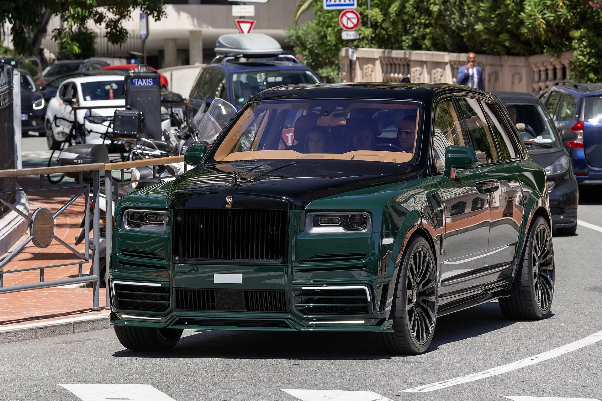 Dark green Rolls-Royce Cullinan with Mansory widebody kit and black wheels, front view on a street