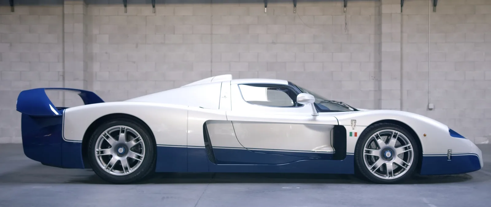 Maserati MC12 Stradale side profile showing the long white-and-blue body, twin-spoke wheels and full-width rear wing