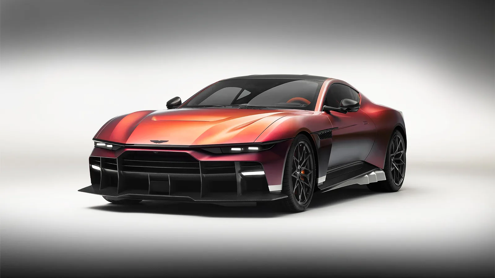 Aston Martin Valen front three-quarter view with headlights on, showing the color-shifting Andromeda Red paint and full carbon front splitter