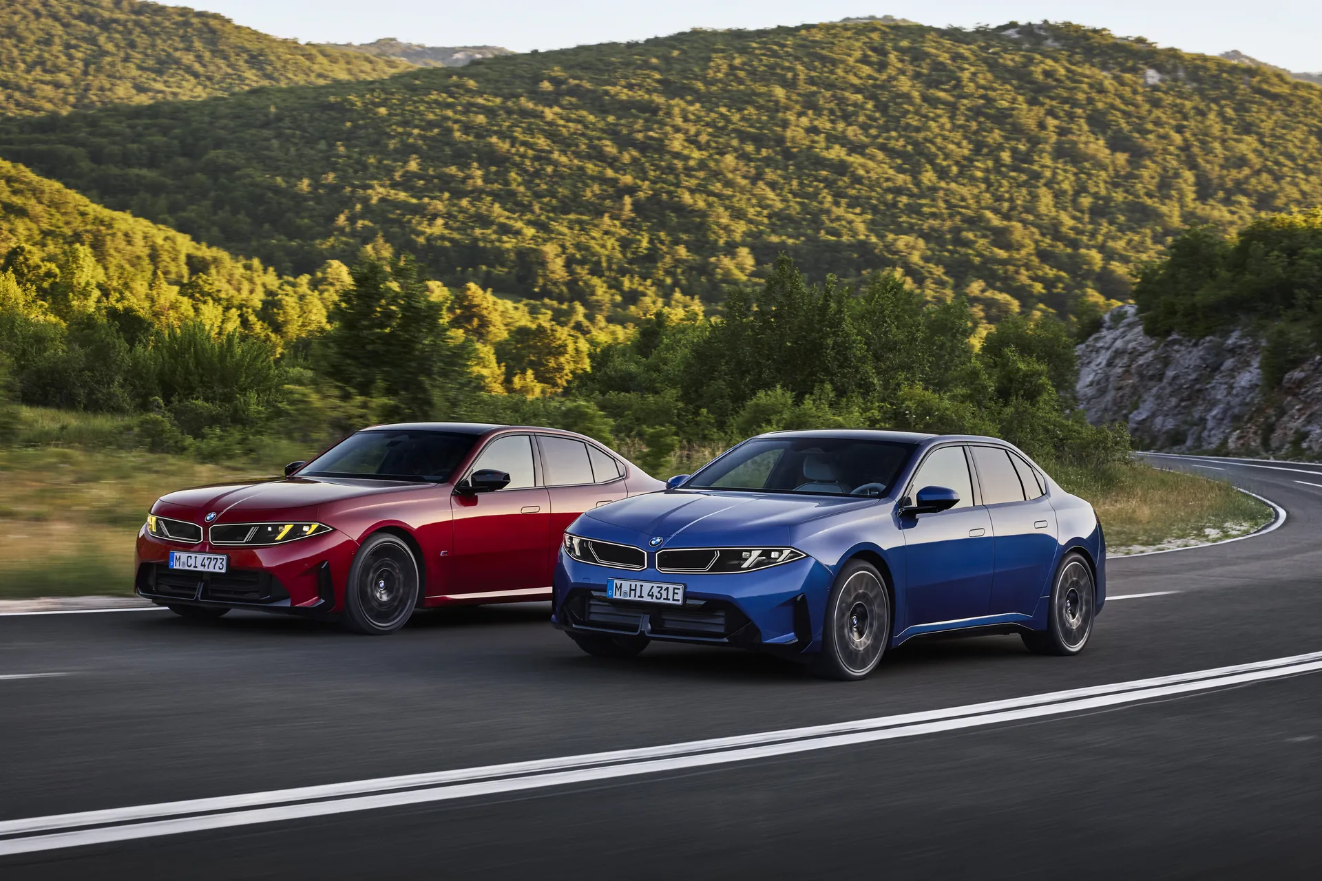 Red and blue new BMW 3 Series G50 sedans driving on a winding mountain road