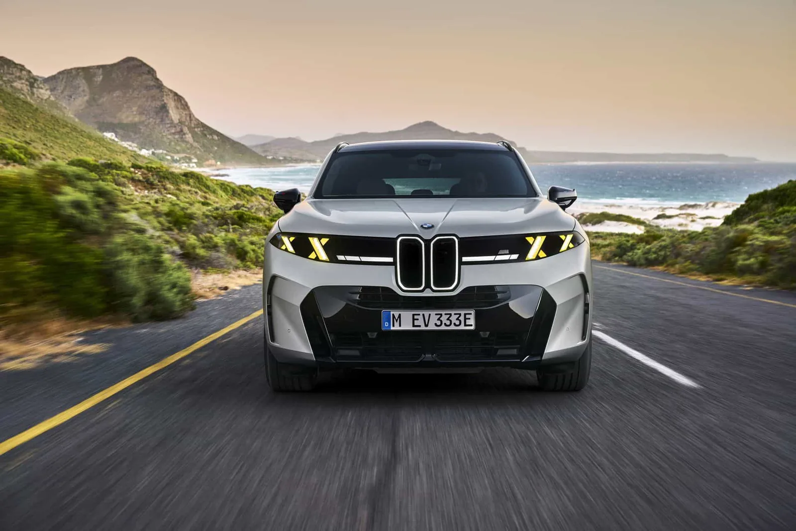 2027 BMW X5 M60e xDrive front — beefier bumpers, yellow M Performance double-X motif in the headlights, illuminated vertical kidney grille