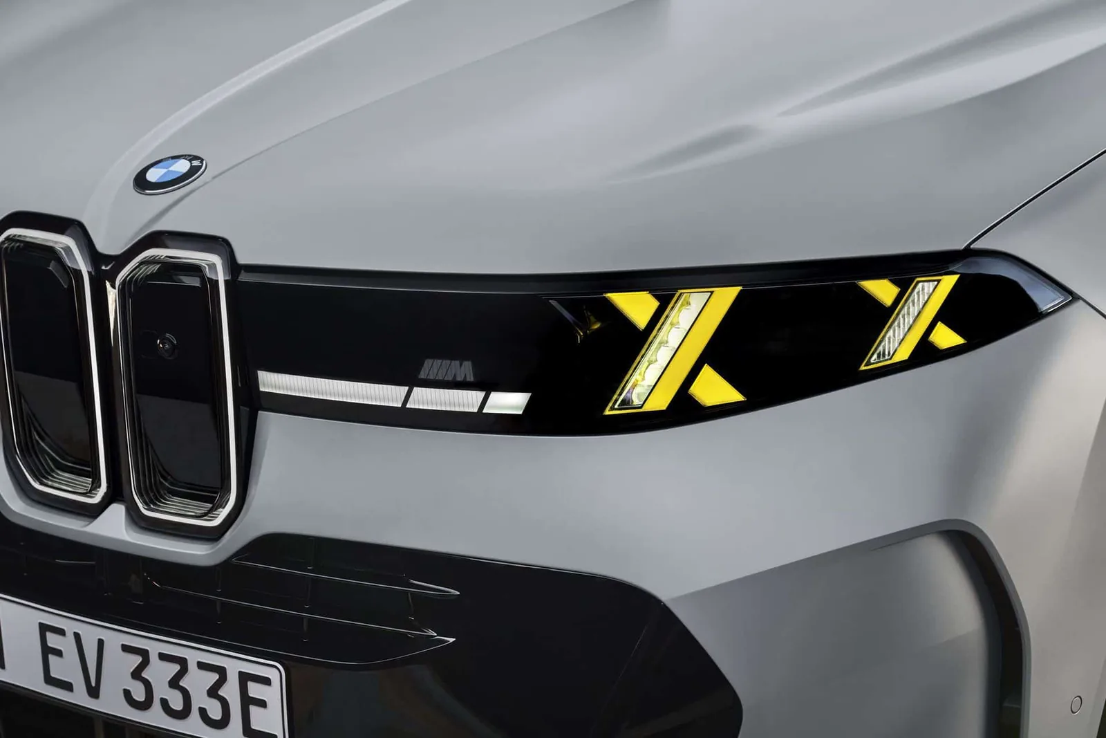 2027 BMW X5 M60e xDrive rear — quad exhaust tips, full-width taillight bar bisected by the illuminated BMW roundel, M badge on the door