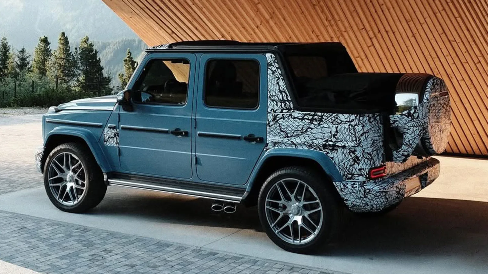 Mercedes-AMG G63 Cabriolet 2026 rear three-quarter view with soft top down, showing spare-wheel-mounted third brake light and full-width rear roll bar