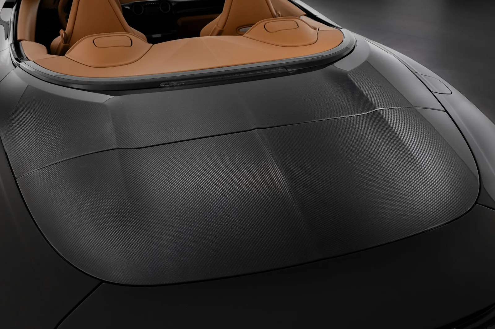 Brabus Bodo Cabriolet carbon fibre tonneau cover close-up with soft top stowed underneath, showing exposed pre-preg carbon weave and precise panel fit