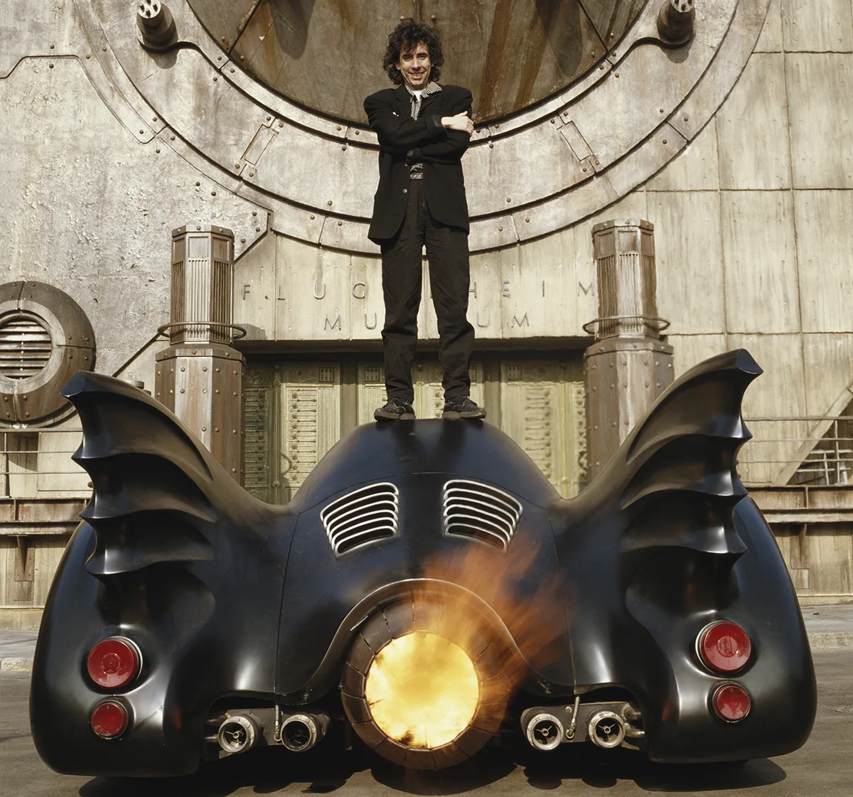 1989 Tim Burton Batmobile designed by Anton Furst — long matte-black bodywork with rounded fenders, exposed turbine intake, twin afterburner exhaust and bat-head hood ornament, parked on a Pinewood Studios soundstage during Batman production