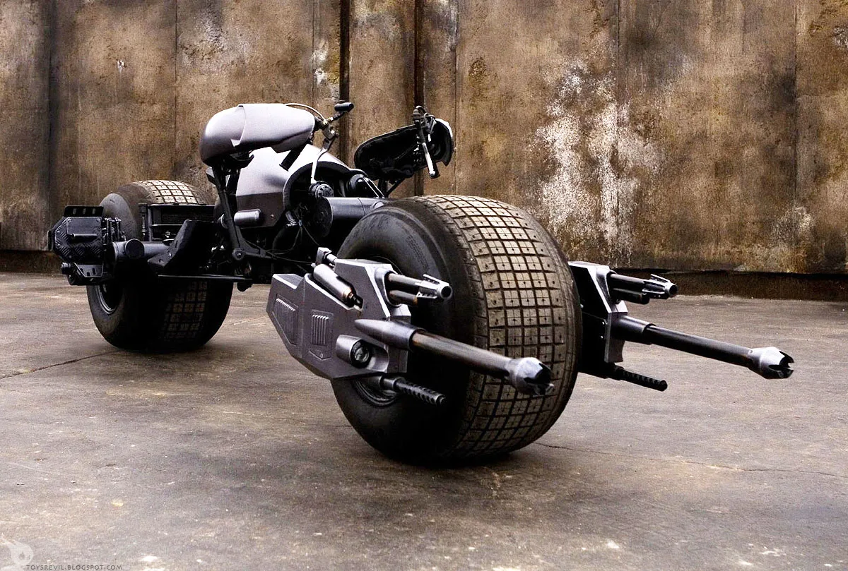 The Batpod motorcycle from The Dark Knight — black emergency-ejection bike powered by a Honda CRF450R single-cylinder engine, controlled by shoulder-mounted handlebars rather than handgrips, with twin grappling-hook cannons mounted to the front forks