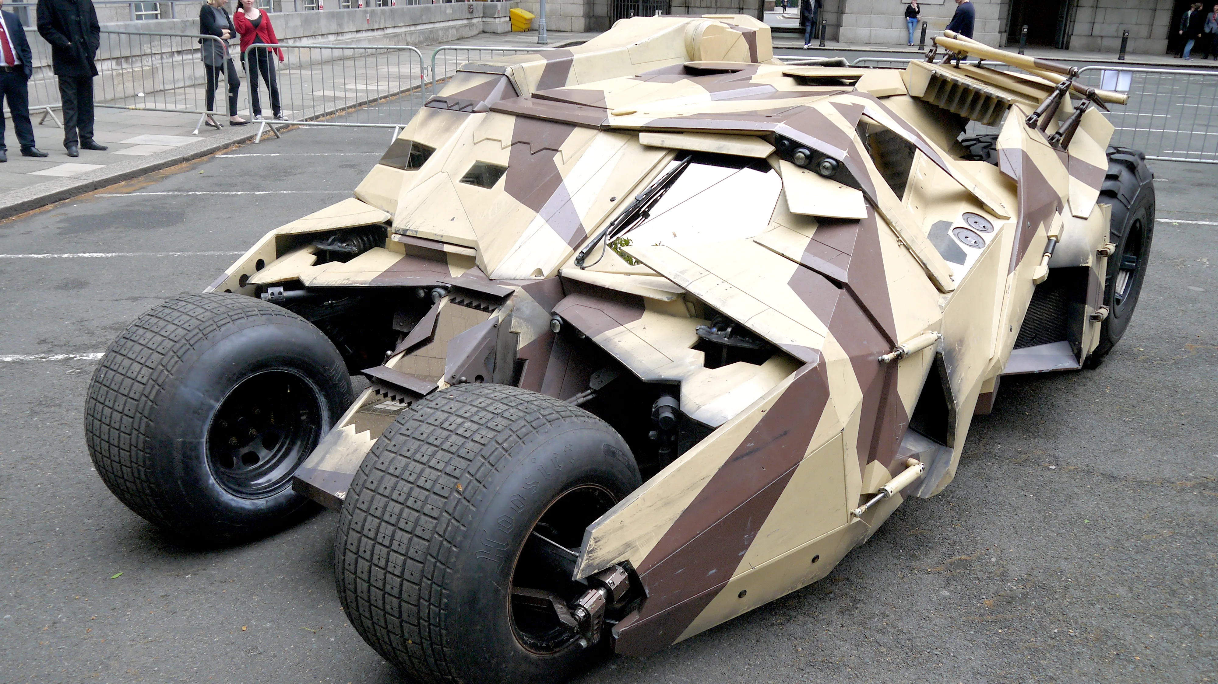 The Tumbler from Christopher Nolan's Dark Knight trilogy — matte-black brutalist armored vehicle with massive 44-inch Super Swamper rear tires, exposed front cantilever wheels, military-spec angular bodywork designed by Nathan Crowley as a fusion of Lamborghini Countach and Humvee