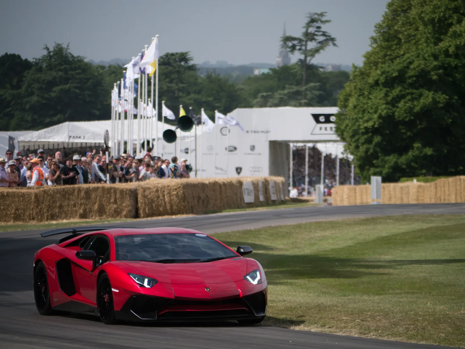 Lamborghini Aventador LP750-4 Super Veloce in red running at Goodwood, front three-quarter action view showing the carbon splitter and Y-shaped daytime running lights