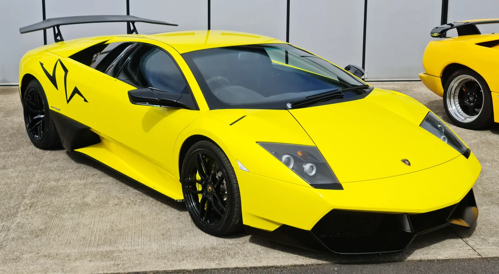 Lamborghini Murcielago LP670-4 SuperVeloce in yellow, front three-quarter view showing the fixed Aeropack rear wing, black SV side graphic and carbon front splitter