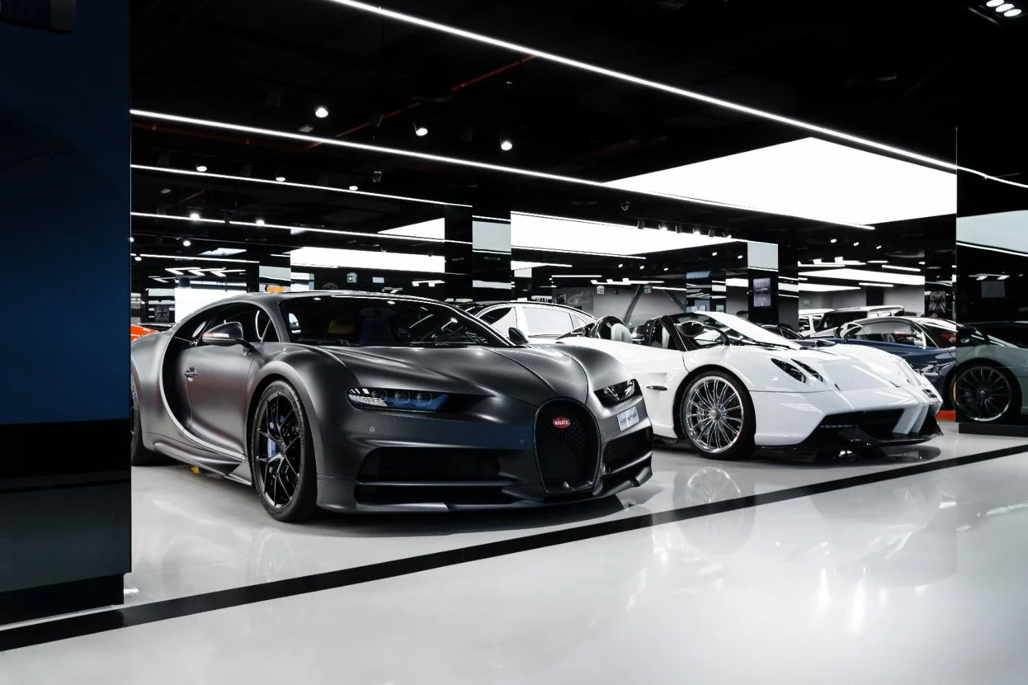 Bugatti Chiron in matte gray parked beside white Pagani Huayra Roadster on the F1rst Motors Dubai showroom floor