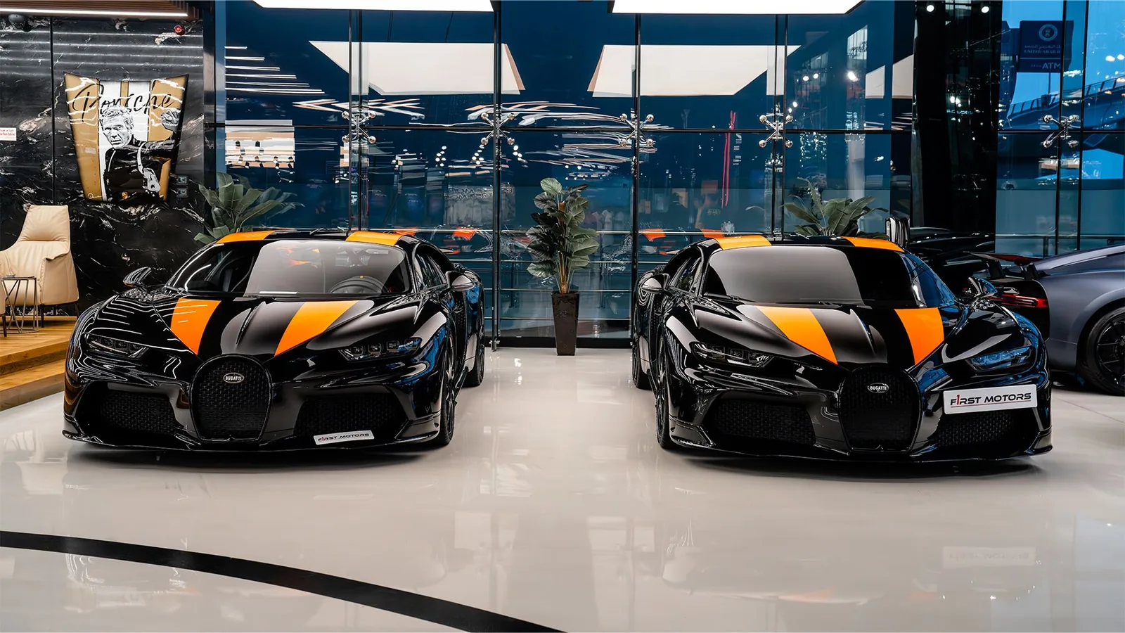 Two Bugatti Chiron Super Sport 300+ hypercars painted matte black with orange stripes parked inside F1rst Motors Dubai showroom
