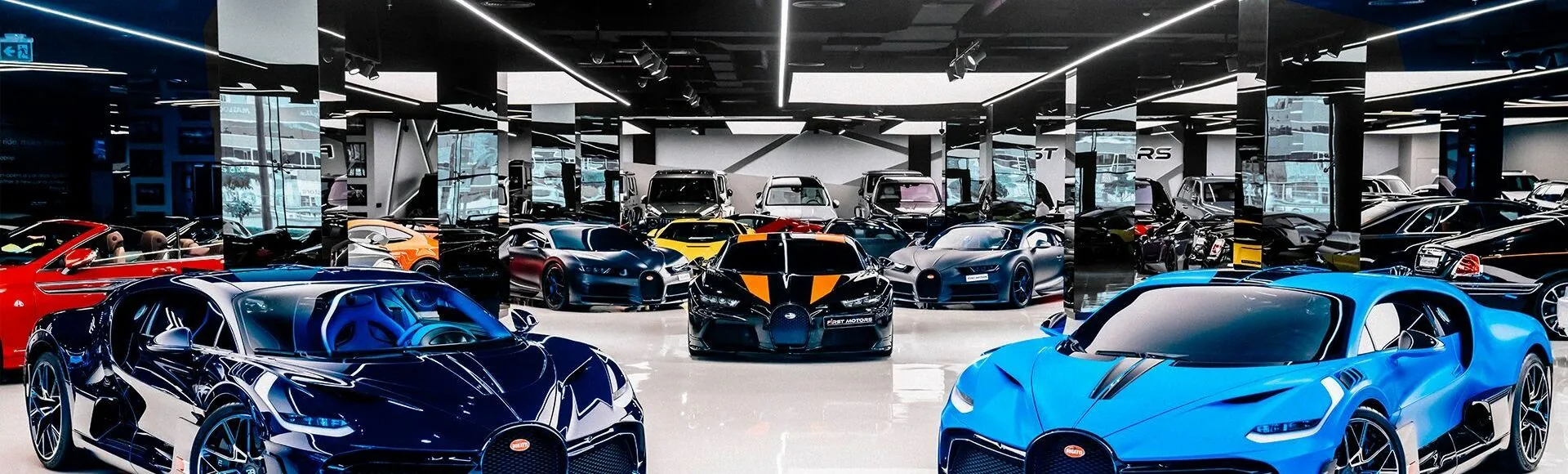 Panoramic view inside F1rst Motors Dubai showroom showing Lamborghini Aventador SVJ Roadster and Bugatti hypercar fleet lined along the exhibit floor