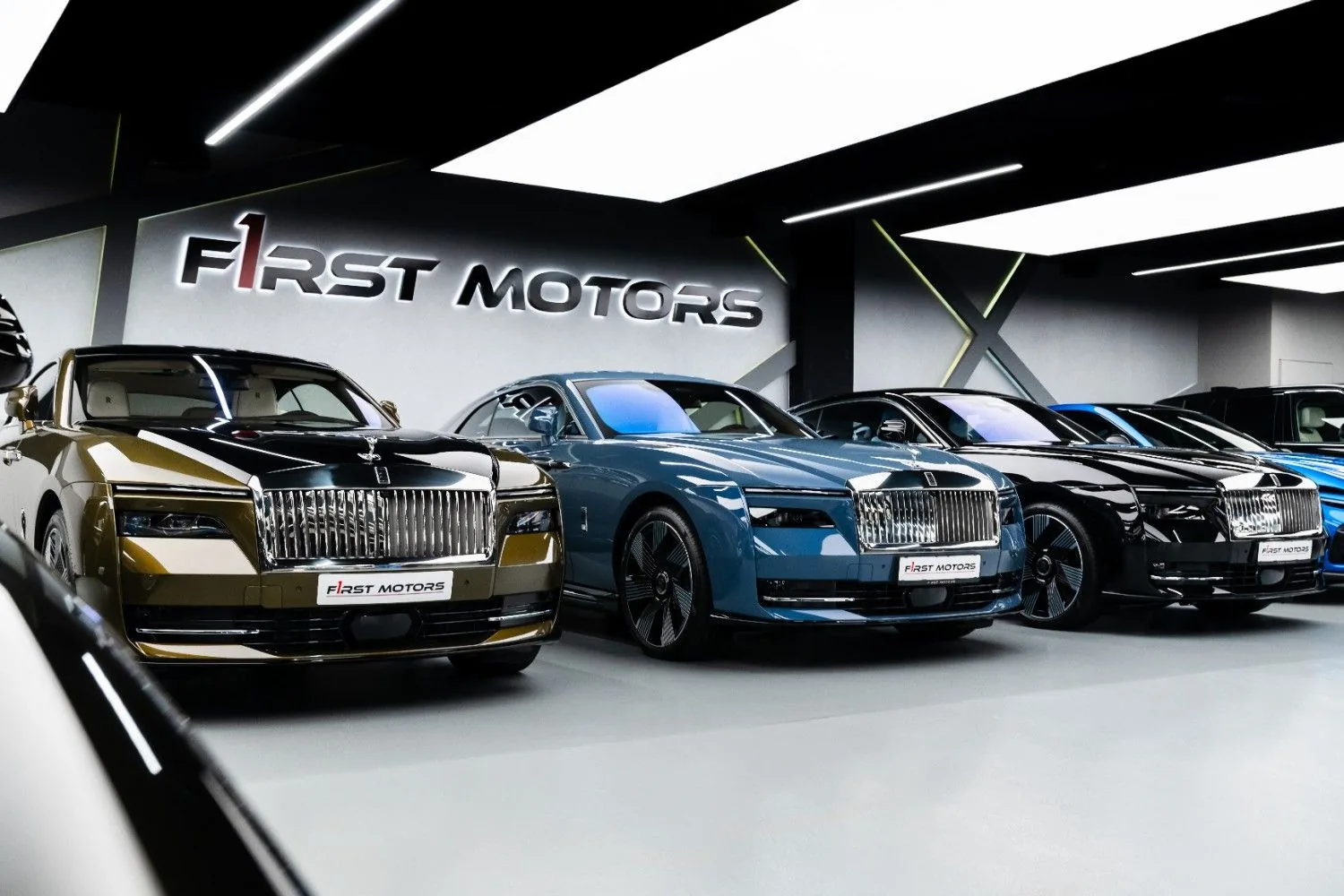Three Rolls-Royce Spectre electric coupes in gold, blue and black parked in line under the F1RST MOTORS wordmark at the Dubai showroom