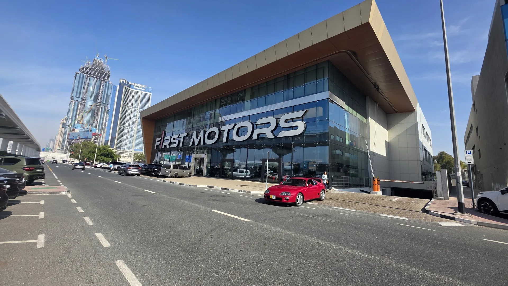 F1rst Motors building on Sheikh Zayed Road with Dubai Marina skyline in the background, entrance ramp and sports cars parked along the street