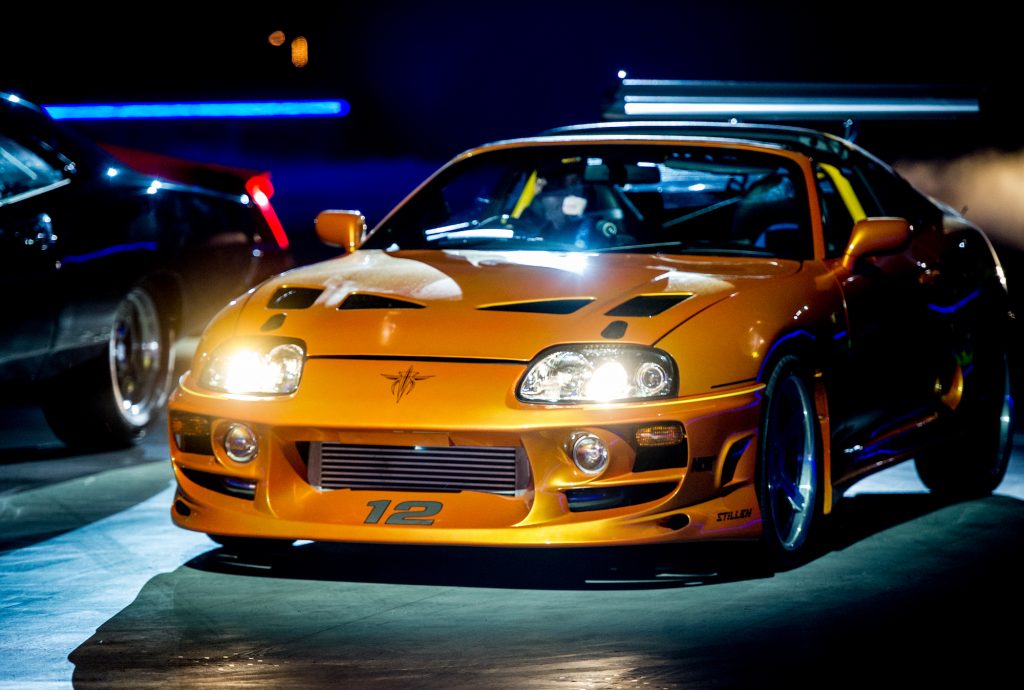 Orange Fast and Furious Supra displayed under dark exhibition lighting