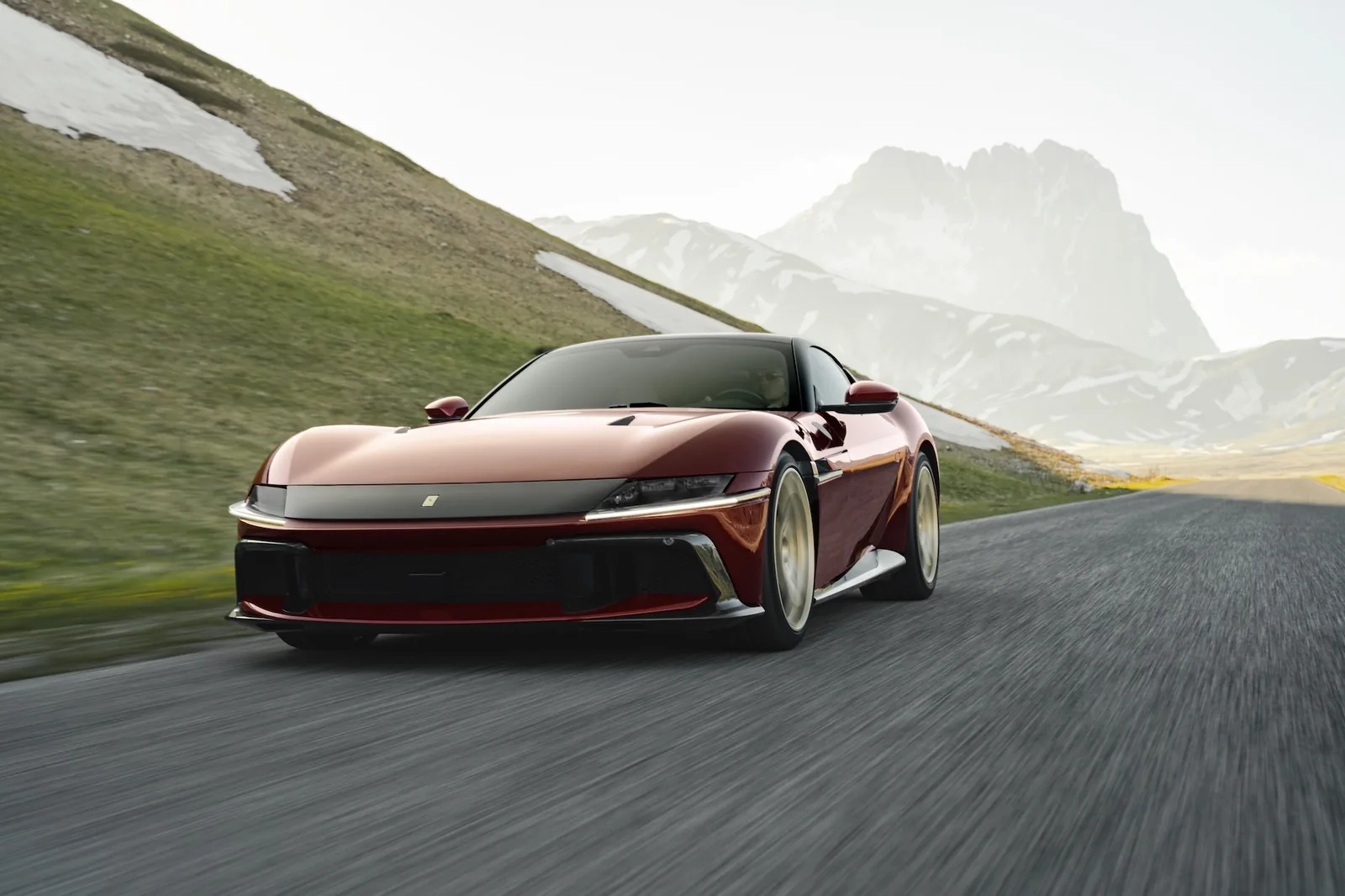 Ferrari 12Cilindri Manuale front three-quarter driving — Rosso Rubino paint, gold wheels, mountain road