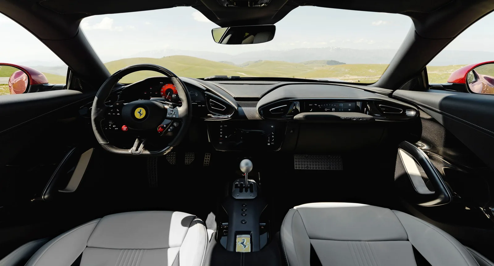Ferrari 12Cilindri Manuale full cabin view through windscreen — white leather seats, mountain landscape, gated shifter visible