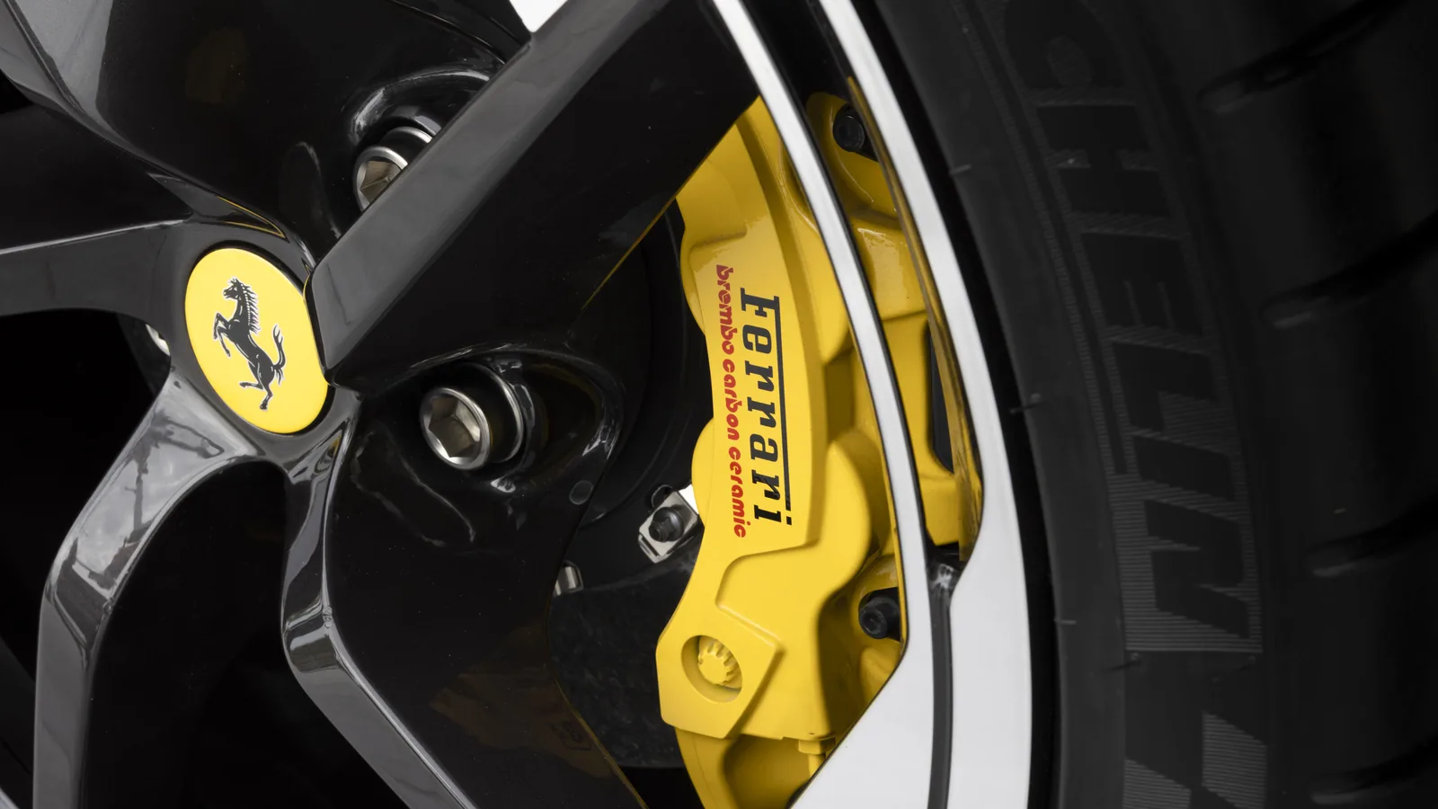 Ferrari HC25 front wheel close-up — yellow Brembo carbon-ceramic caliper with red Ferrari script, prancing horse centre cap on the matte-black five-spoke wheel, Michelin Pilot Sport tyre sidewall