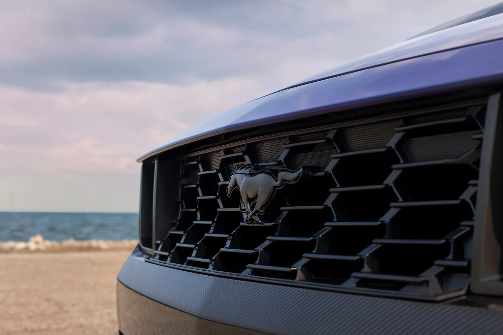 Close-up of the Ford Pony badge and honeycomb grille on the 2027 Ford Mustang Dark Horse SC Convertible in Precision Purple, with lakeshore in the background