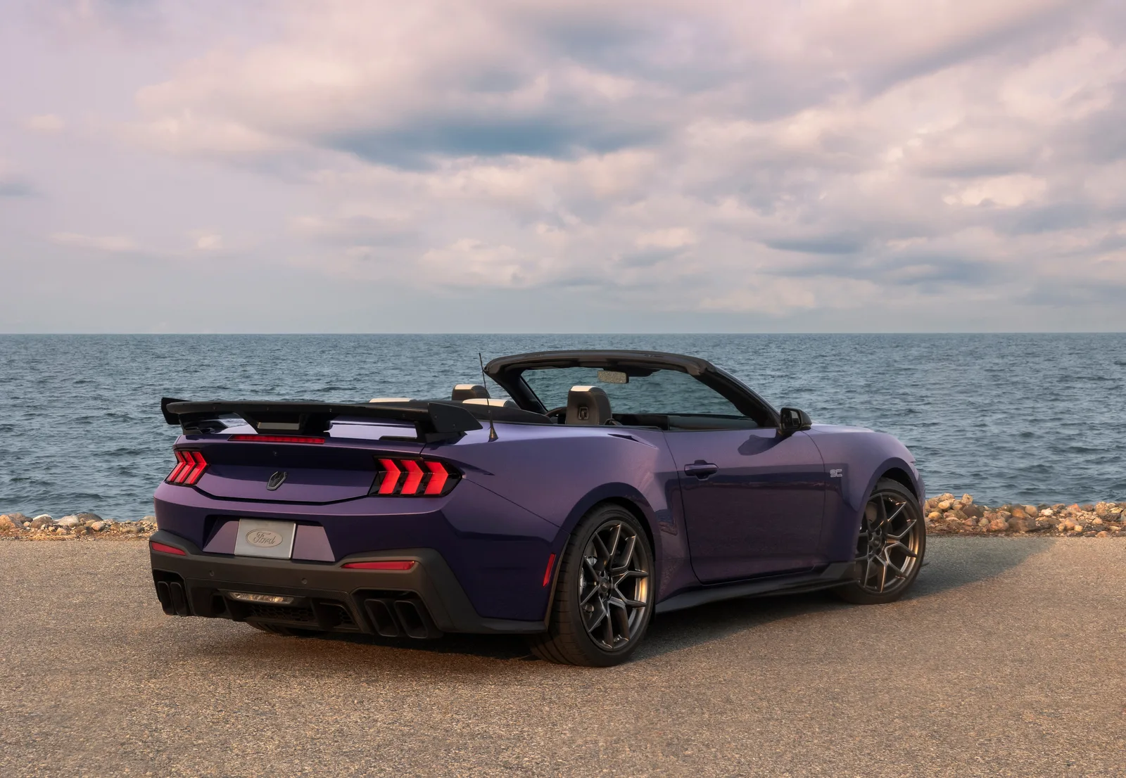 2027 Ford Mustang Dark Horse SC Convertible rear three-quarter static view along lakeshore in Precision Purple showing rear diffuser, quad exhaust and full-width taillight bar