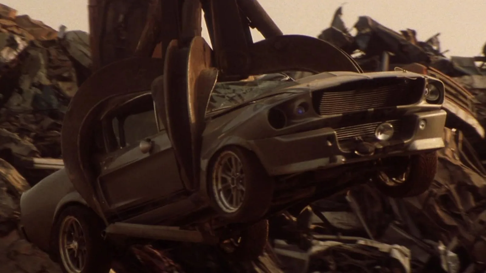 Ford Mustang Eleanor lifted by a junkyard crane grabber in Gone in 60 Seconds 2000, dramatic final-act scrapyard scene with damaged pepper-grey Shelby GT500 tribute