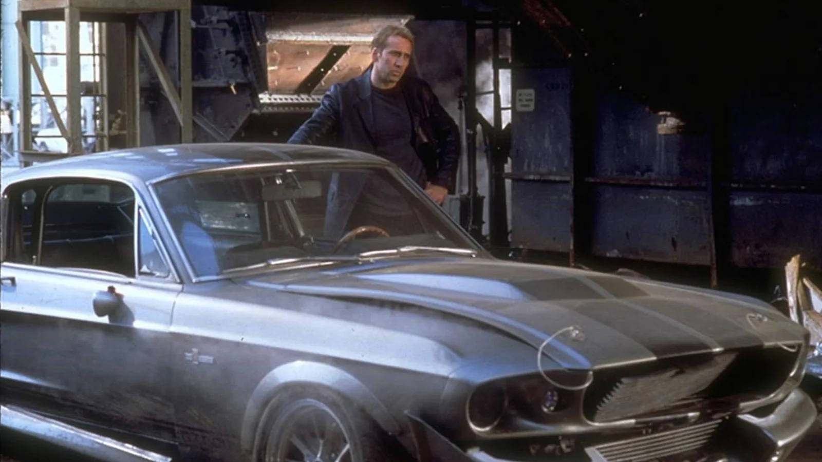 Nicolas Cage as Memphis Raines standing next to the pepper-grey 1967 Ford Mustang Eleanor in the workshop reveal scene from Gone in 60 Seconds 2000