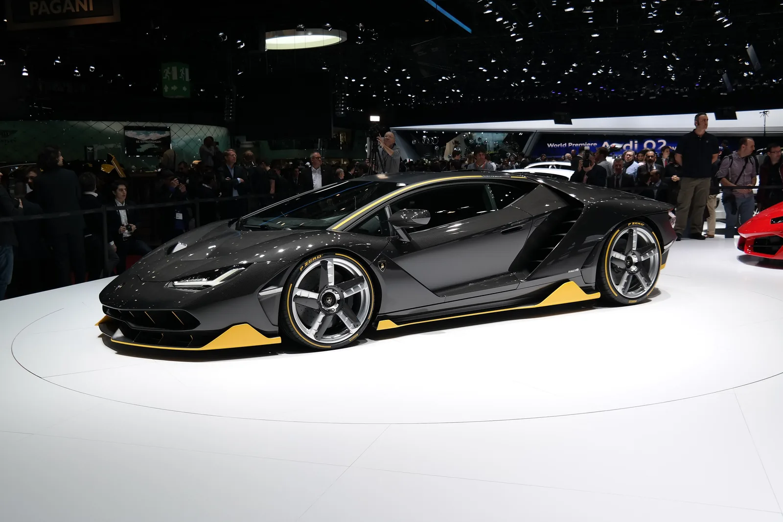 Lamborghini Centenario side profile on the Geneva Motor Show stand, showing the carbon fibre monocoque proportions and yellow accents