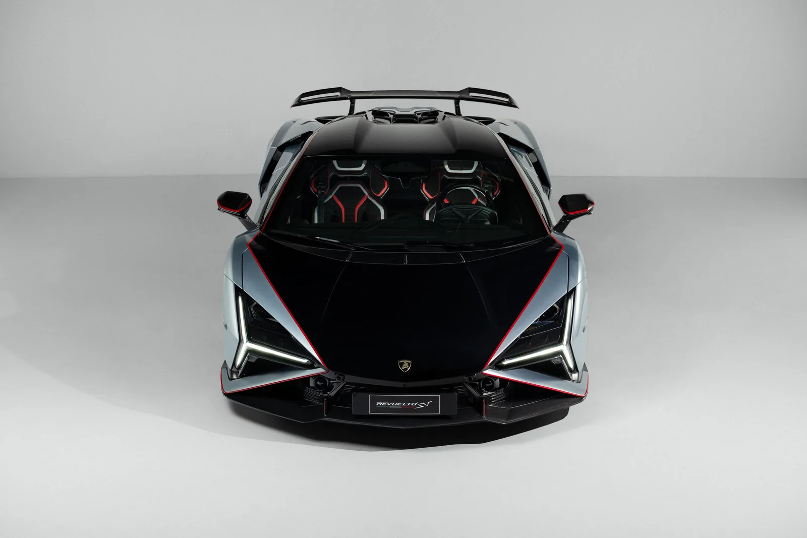 Lamborghini Revuelto SV head-on front view showing full-width aero package: sculpted carbon splitter, Y-signature LED daytime running lights, black carbon hood with red pinstripe running the entire length and central Lamborghini shield behind the windscreen