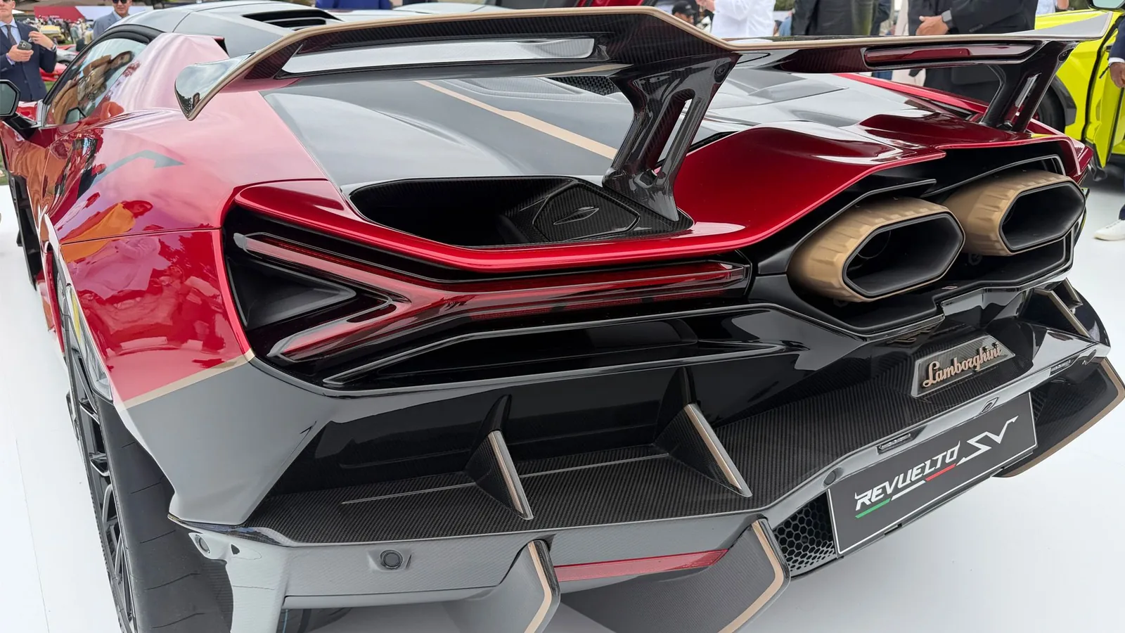 Lamborghini Revuelto SV rear end close-up showing dual gold-anodised exhaust tips, exposed carbon diffuser fins, hexagonal LED tail-light signature and REVUELTO SV licence-plate frame