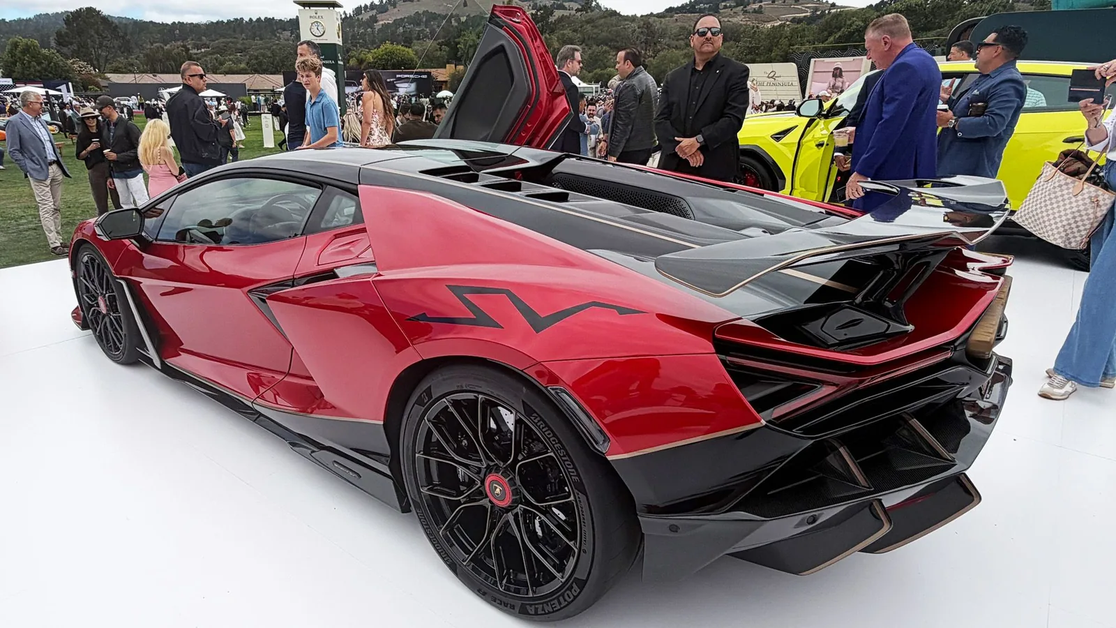 Lamborghini Revuelto SV rear three-quarter view at Pebble Beach concourse showing the Nera Red launch livery, exposed carbon SV badge across the buttress and quad-exit gold-anodised exhaust