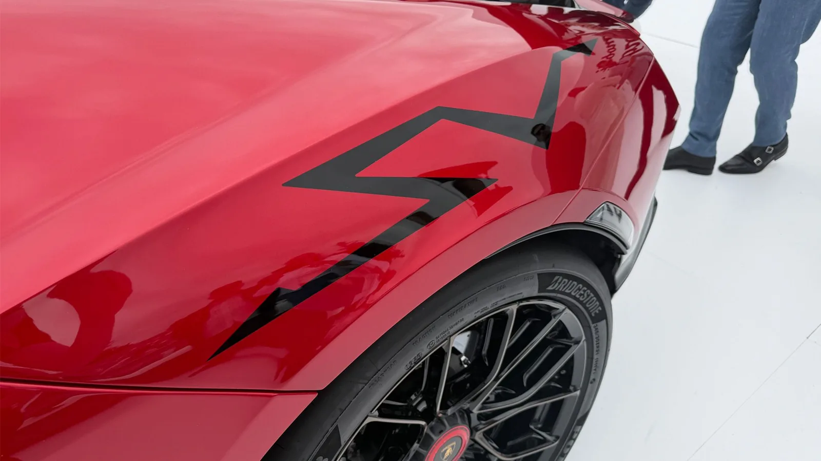 Lamborghini Revuelto SV side flank close-up showing large black SV nomenclature graphic across Nera Red carbon rear haunch and forged multi-spoke wheel with Bridgestone Potenza Race R tyre