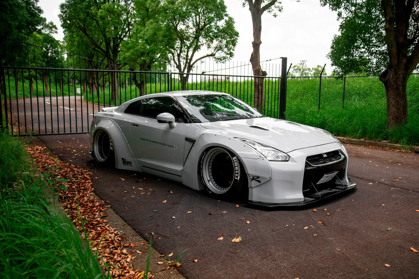 Liberty Walk LB-Works Nissan GT-R R35 in silver with bolt-on wide fenders and air suspension on a tree-lined road
