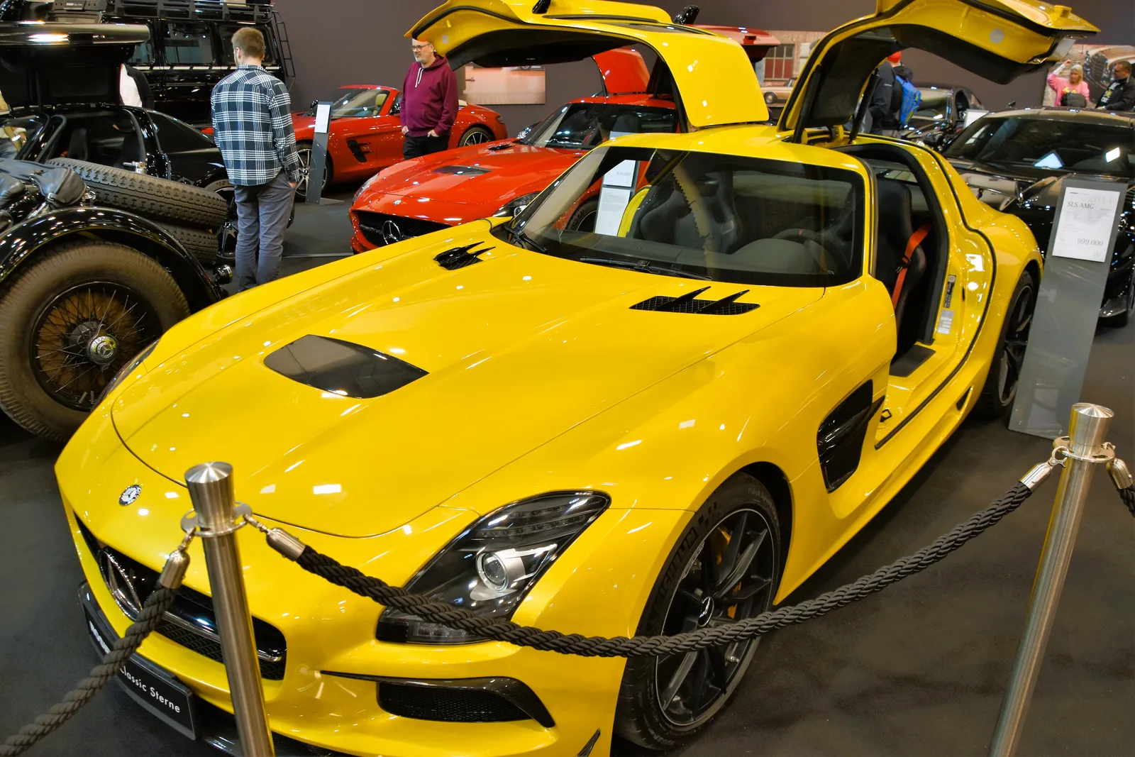 Yellow Mercedes-Benz SLS AMG Black Series with gullwing doors open, front three-quarter view at an auto show