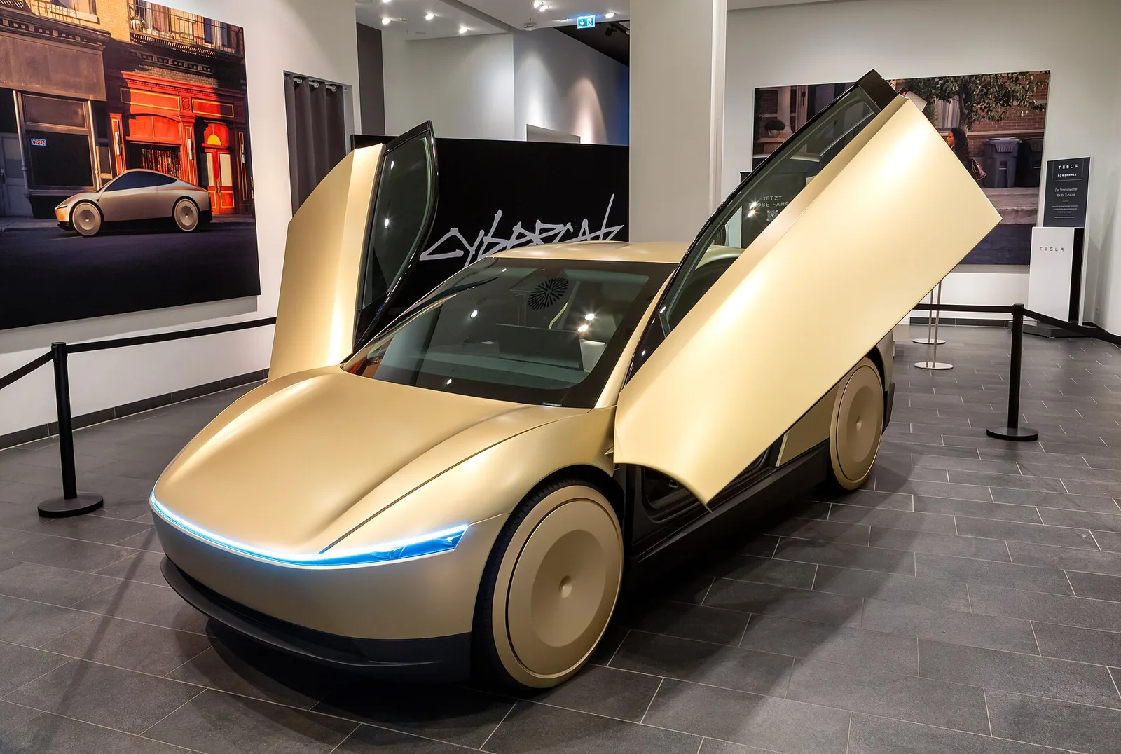 Tesla Cybercab on display at the Mall of Berlin in 2024, with a CYBERCAB wordmark graphic in the background
